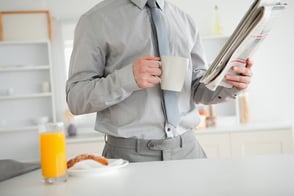 Businessman holding a newspaper while having breakfast in his kitchen.jpeg